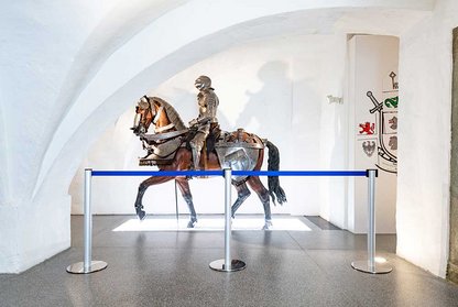 Ausstellungsstück im Museum: Ritter auf Pferd, hinter Absperrpfosten 